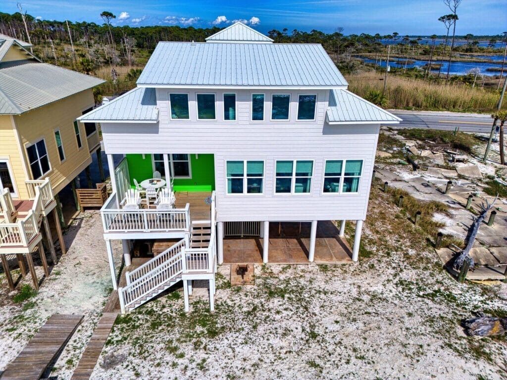 A two-story beachfront house with a covered porch and a small outdoor seating area.