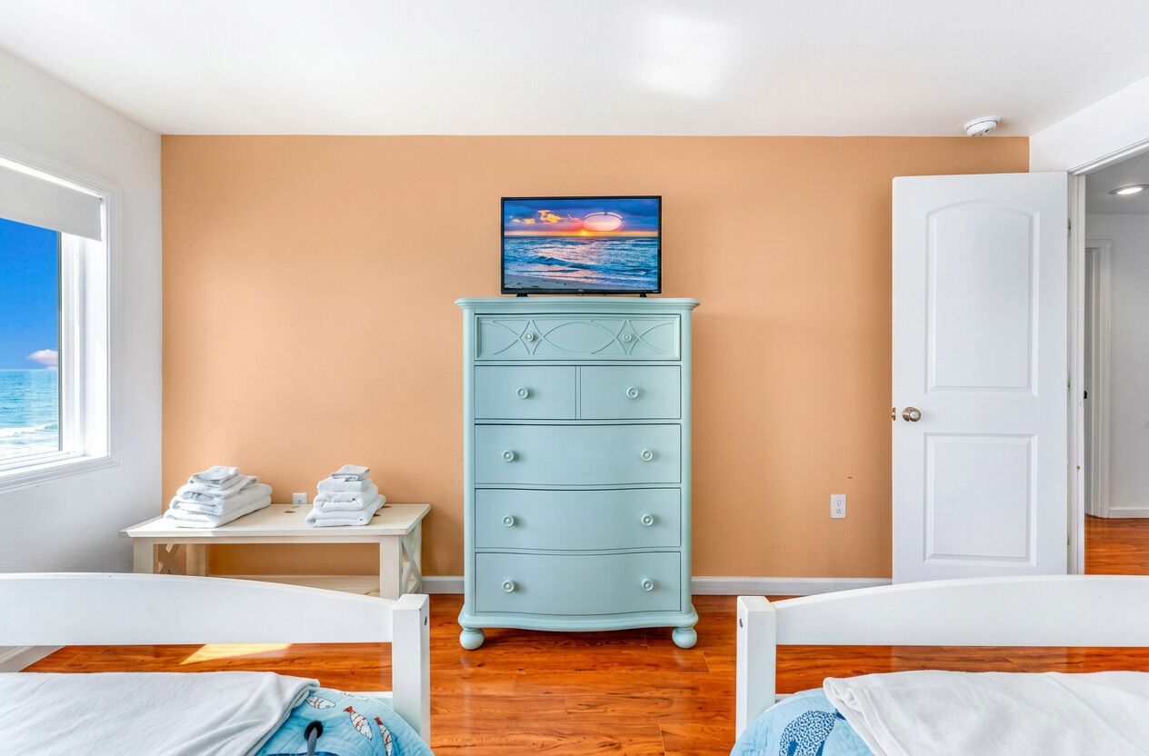 Un dormitorio con cama, cómoda, televisor y vista al mar.