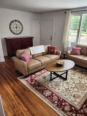 A living room with a beige sofa, a coffee table, a patterned rug, and a wall clock.