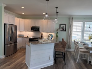 A modern kitchen with stainless steel appliances, white cabinetry, and a dining area with wicker chairs.