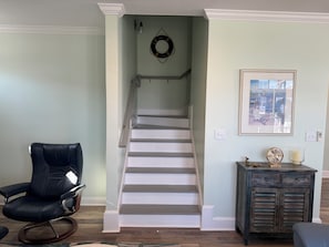A staircase with a white railing, a black leather chair, a dark wooden cabinet, and a framed picture on the wall.