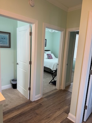 A hallway leading to a bedroom with a bed, a chair, and a trash bin.
