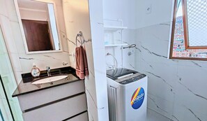 Un baño con lavamanos, espejo, toallero y lavadora empotrada.