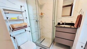 Uma casa de banho moderna com cabine de duche em vidro, sanita branca, lavatório com espelho e toalheiro com toalhas.