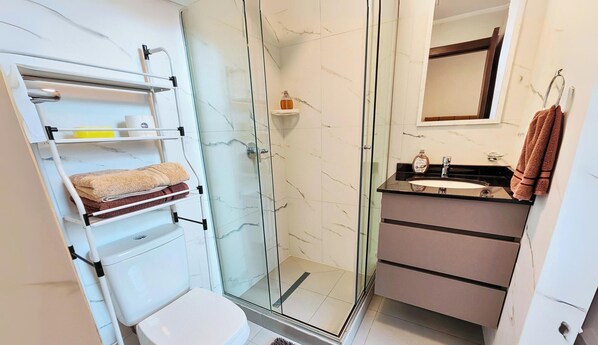 Un baño con cabina de ducha de vidrio, inodoro blanco, lavabo con espejo y barra para toallas.