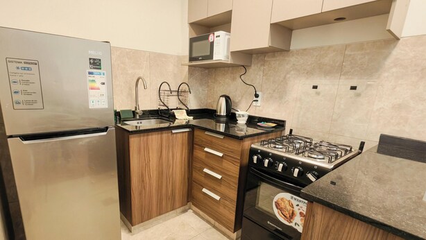 Cozinha compacta com geladeira, fogão, micro-ondas e armários de madeira.