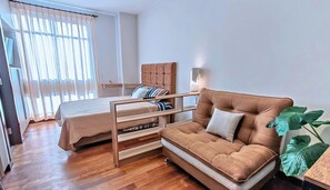 Una habitación con cama, sofá, mesa de madera y una planta grande.