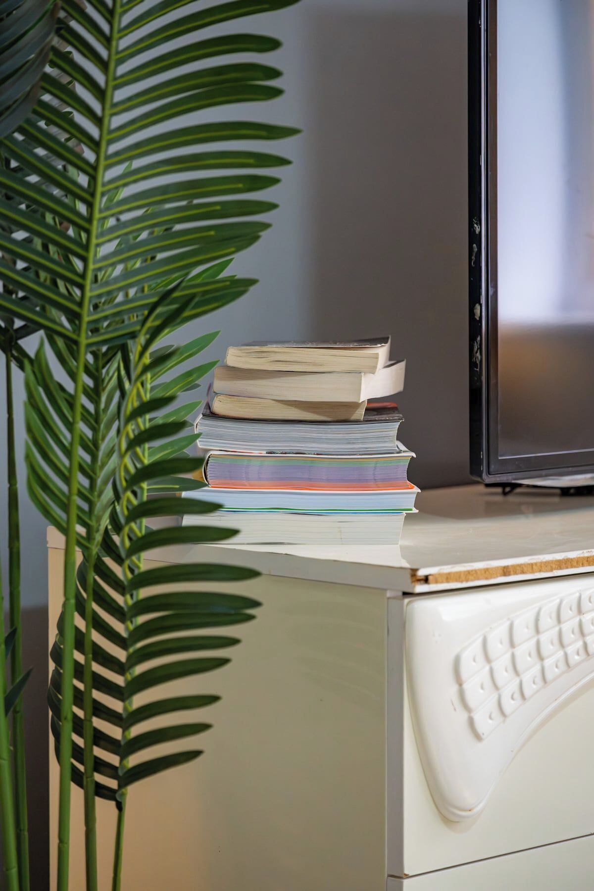 A desk with a stack of books, a keyboard, and a television.