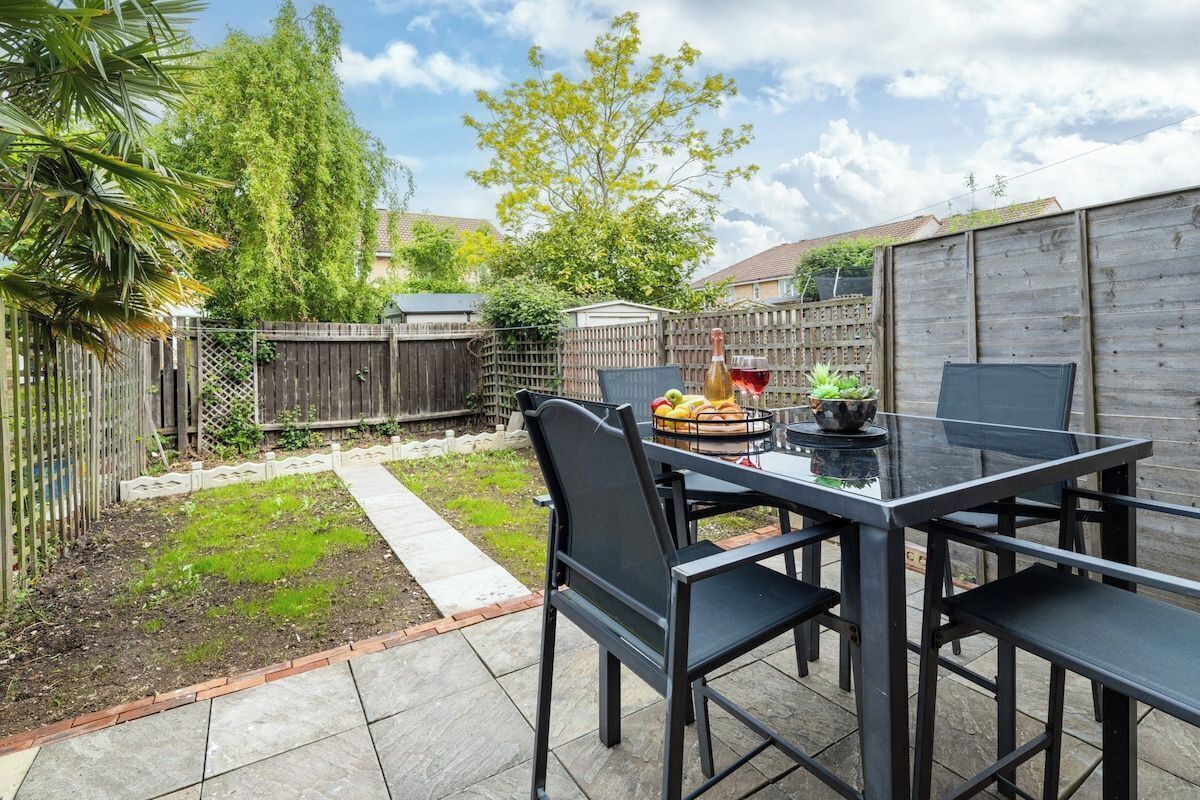 A patio with a table and chairs, surrounded by a wooden fence and greenery.