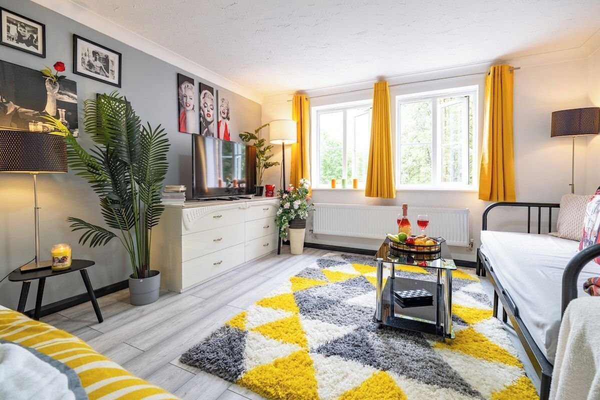 Une chambre moderne avec un lit, une table de chevet, une lampe, une fenêtre avec des rideaux, un radiateur et une plante.