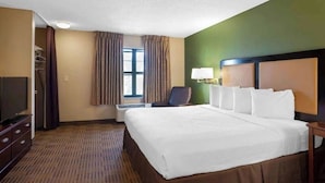 Une chambre d’hôtel avec un grand lit, une télévision, une chaise, un bureau et une fenêtre avec des rideaux.