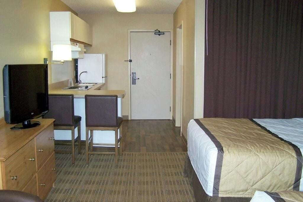 Una habitación de hotel con una cama, un escritorio con una silla, un televisor y una puerta.
