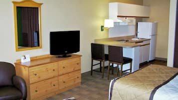 Ein kompaktes Hotelzimmer mit einem Einzelbett, einem kleinen Schreibtisch mit Fernseher, einer Küchenzeile und einem Spiegel.
