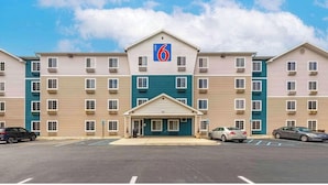A multi-story motel with a central entrance, parking lot, and a clear blue sky. - Motel 6 Suites Birmingham Pelham  AL (Pelham)