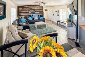 Ein Wohnzimmer mit einer Couch, einem Hocker und einem Couchtisch, einem Kamin und einem an der Wand befestigten Fernseher.