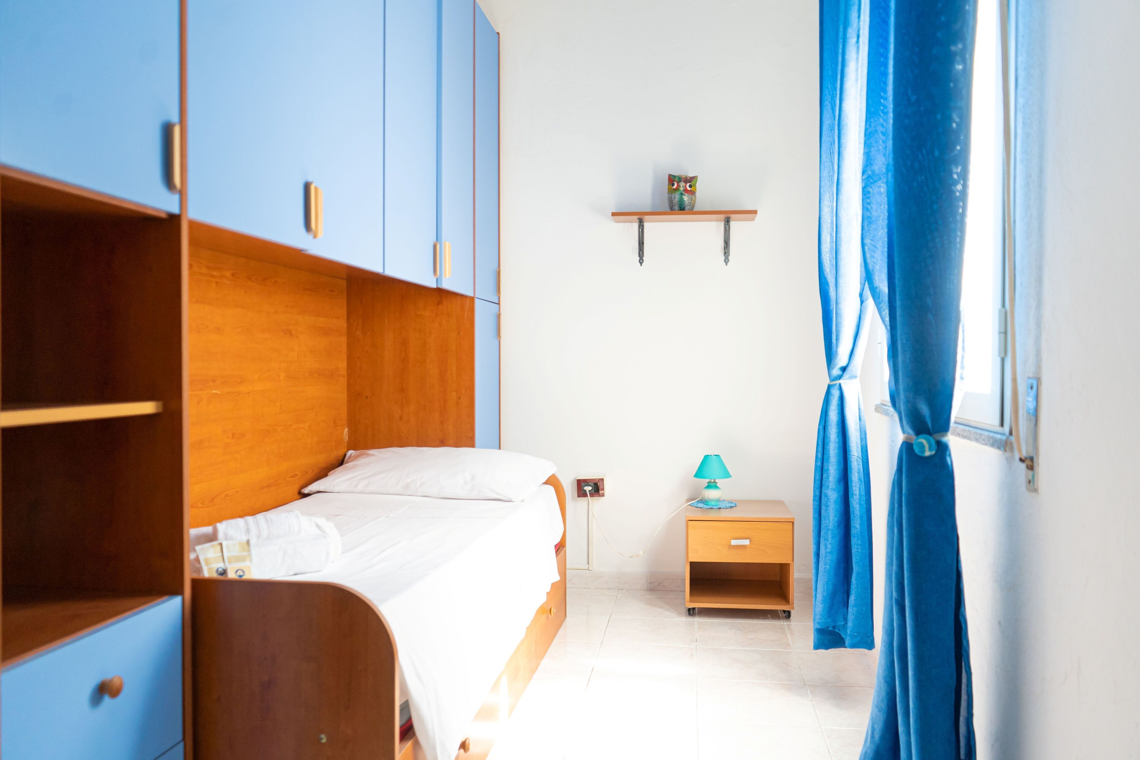 Un dormitorio con una cama de madera, una mesita de noche, una estantería y una ventana con cortinas.
