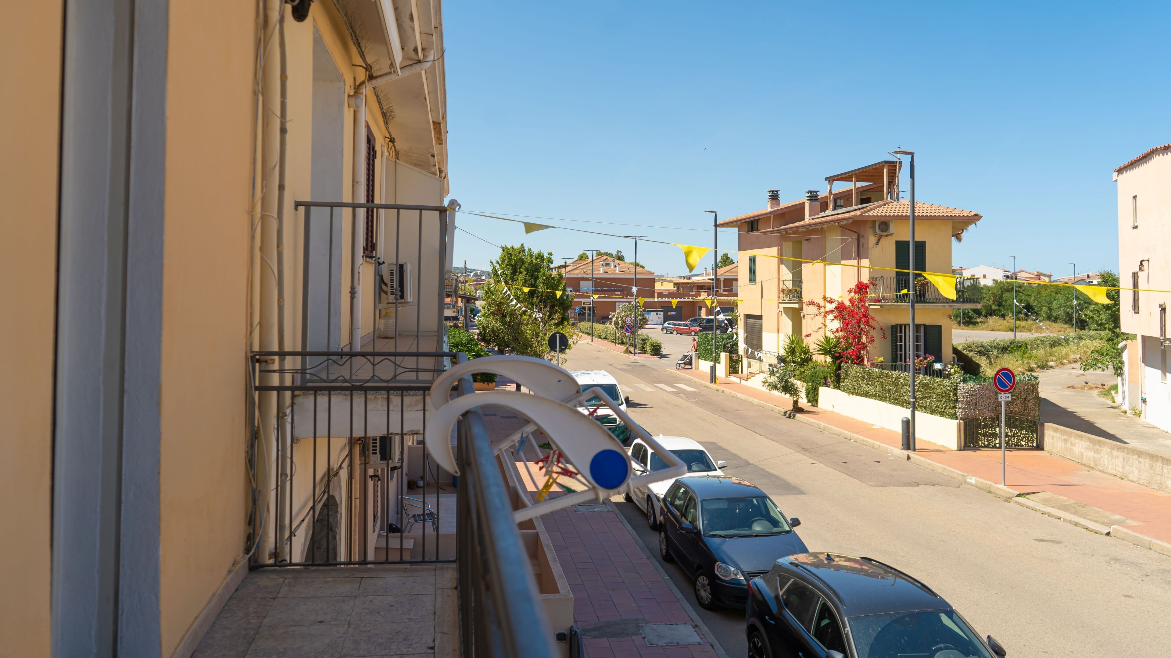 Eine Wohnstraße mit parkenden Autos, blauem Himmel und Häusern mit Balkonen.