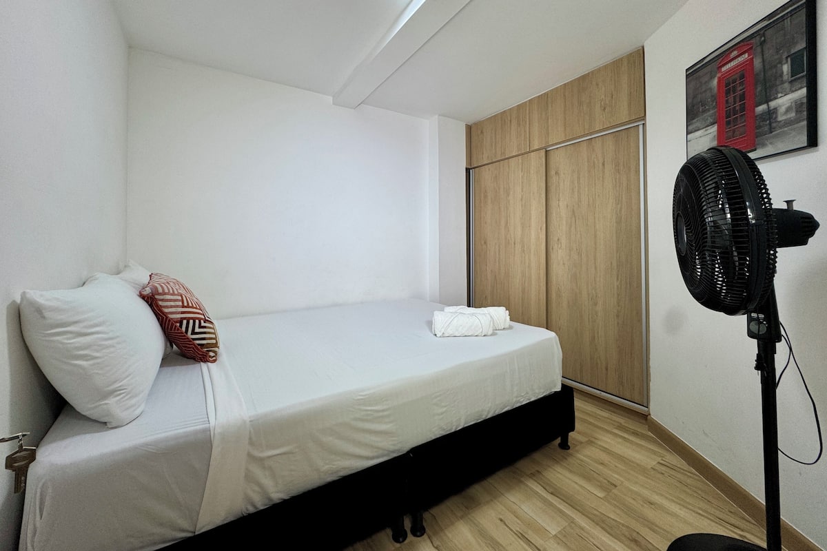 Uma cama de solteiro com colchão branco, cabeceira preta e guarda-roupa de madeira.