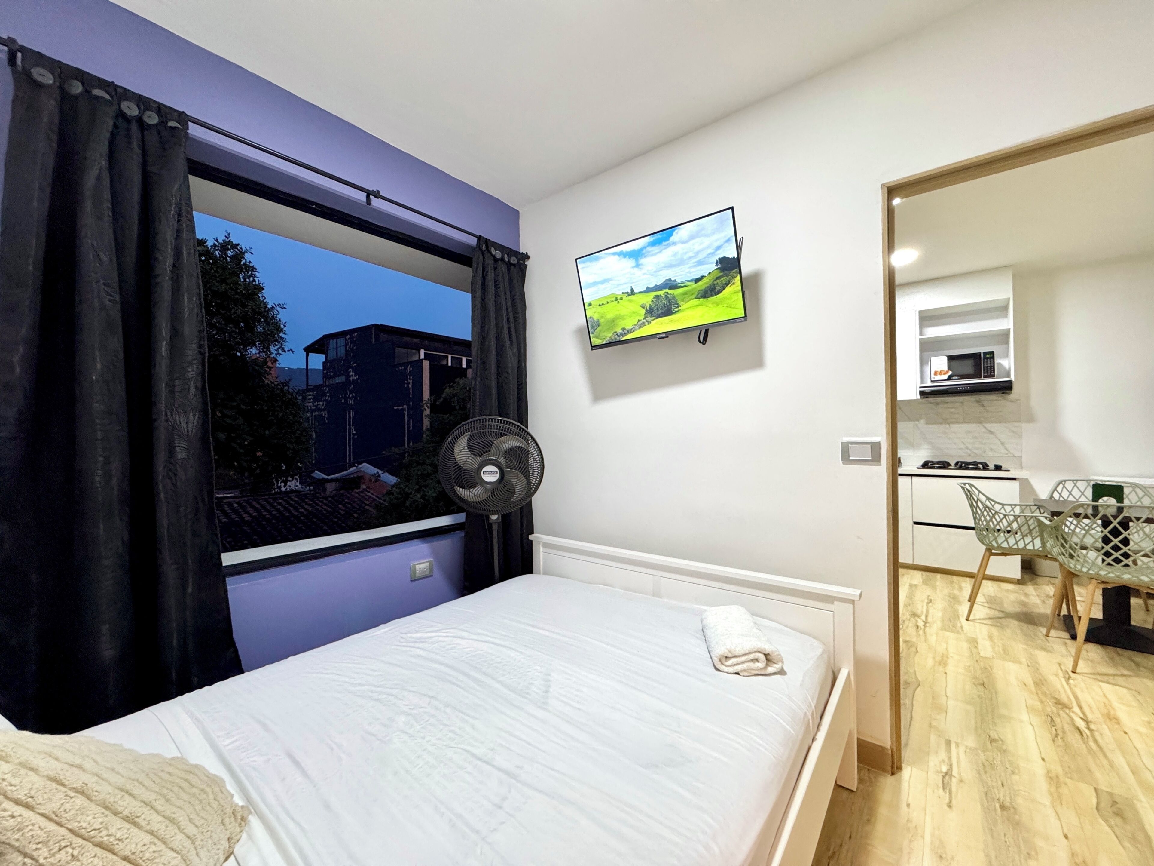 Quarto com cama, televisão na parede, ventilador e vista para o exterior.