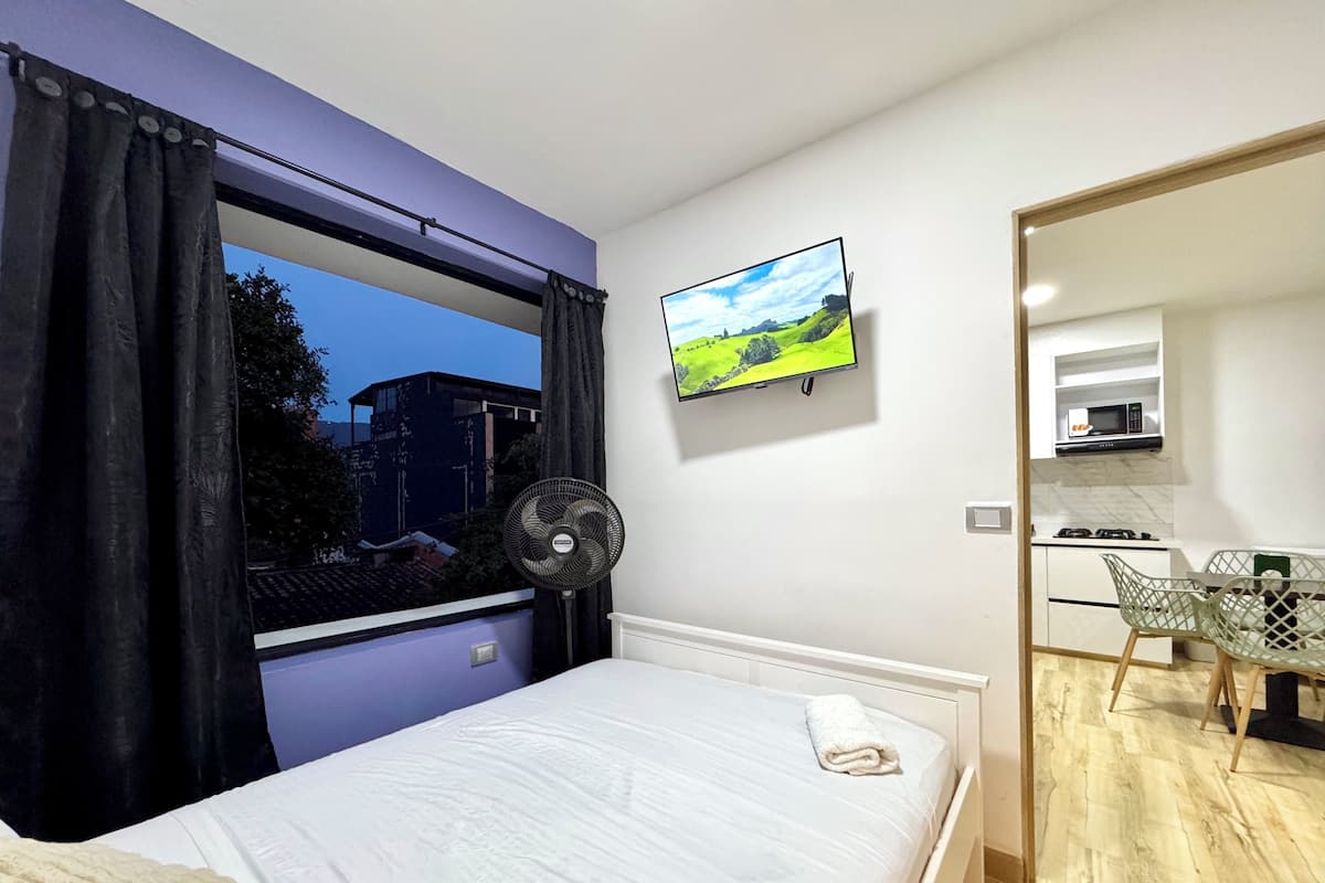 Quarto com cama, televisão na parede, ventilador e vista para o exterior.