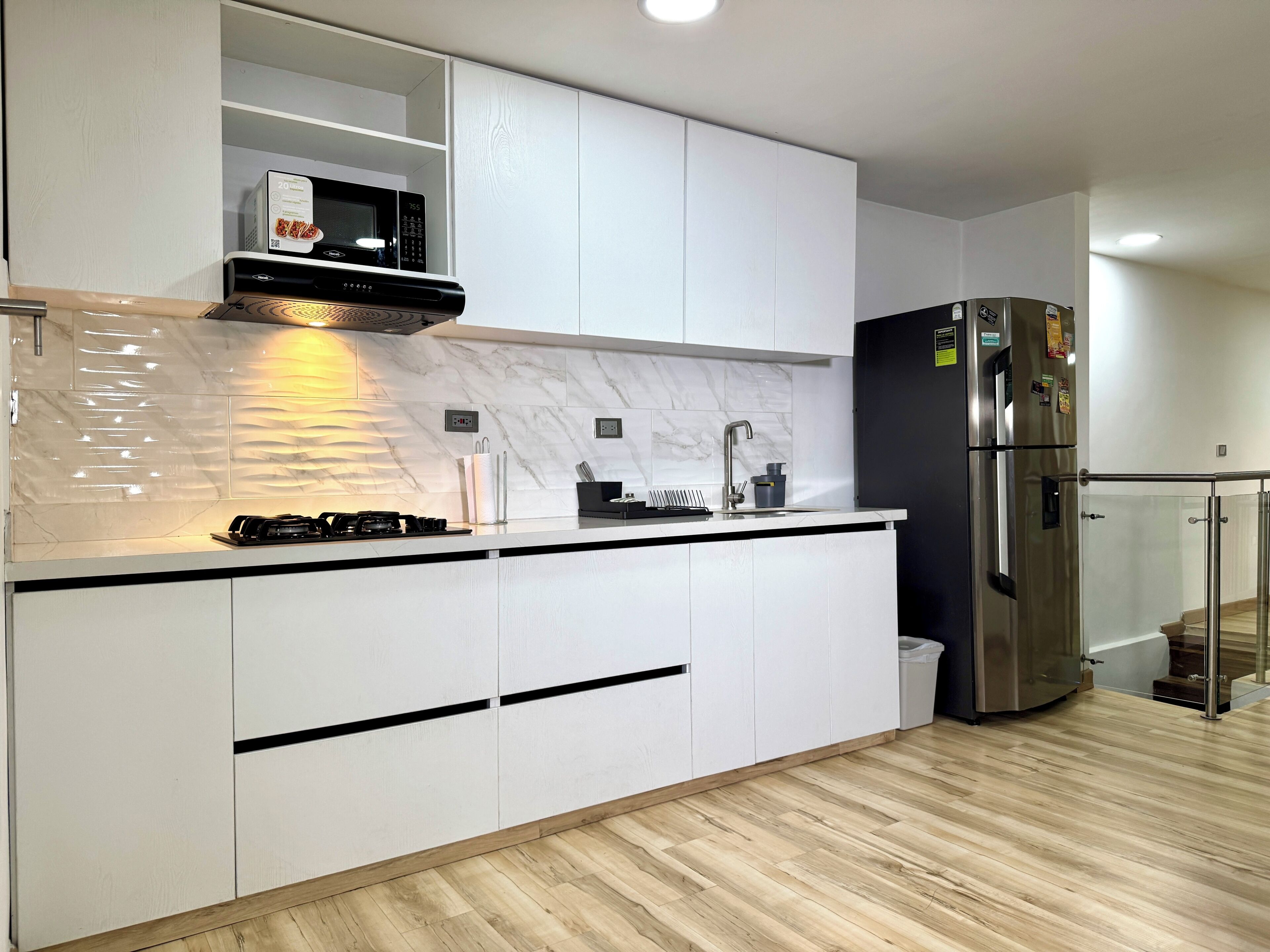 A modern kitchen with white cabinets, a stainless steel refrigerator, a microwave, and a gas stove.