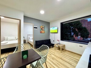 Quarto moderno com cama, sofá, mesa de jantar, televisão e janela com vista para a cidade.