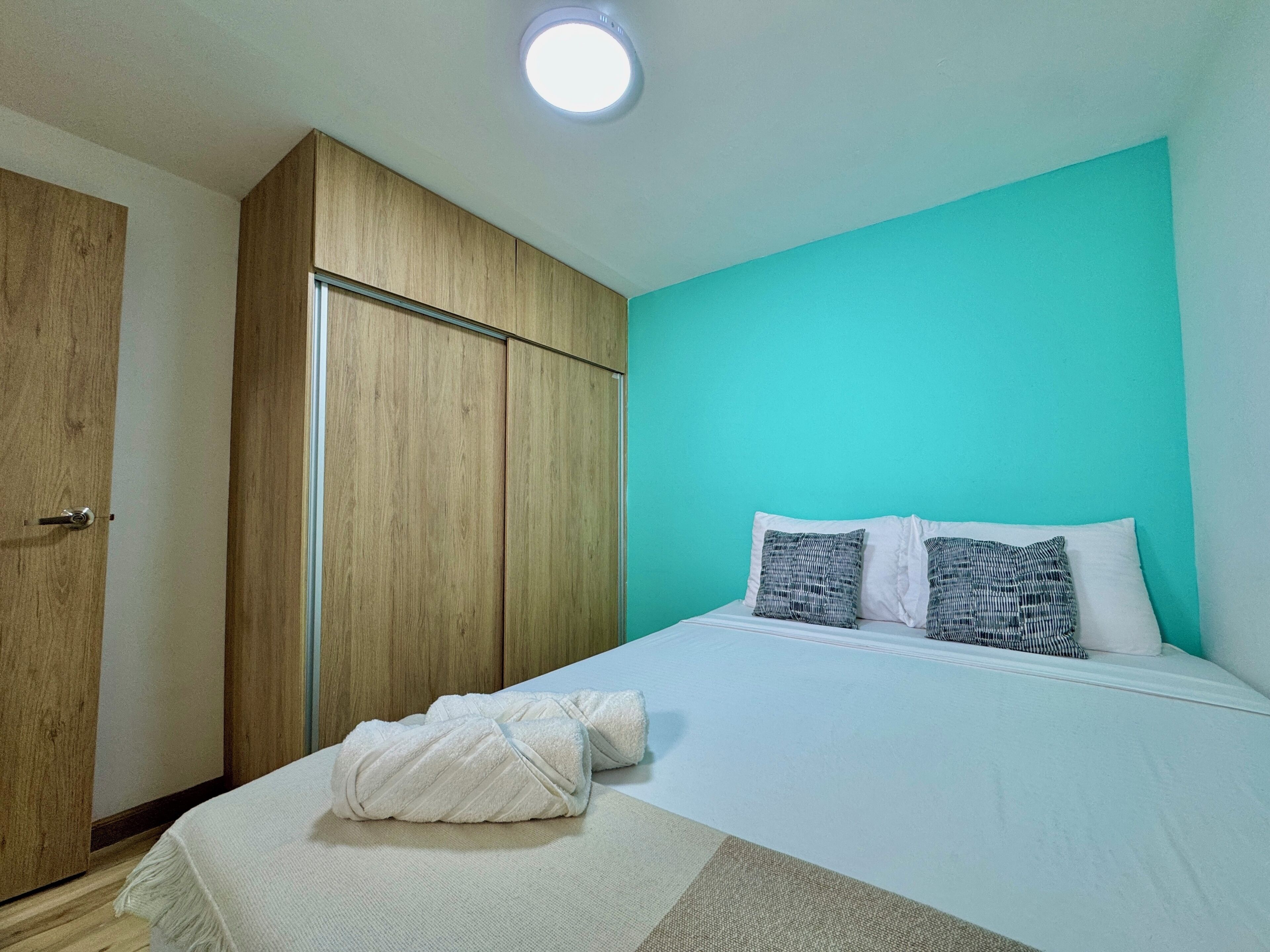 Quarto com cama, almofadas, toalha, guarda-roupa e luz no teto.