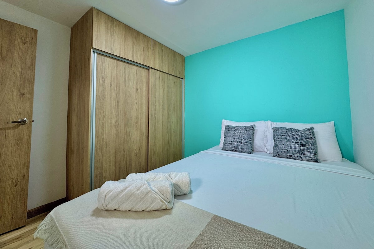 Quarto com cama, almofadas, toalha, guarda-roupa e luz no teto.