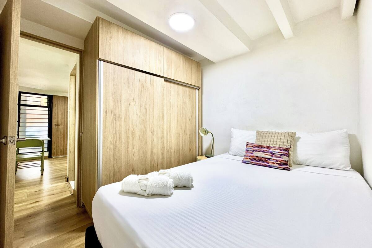 Quarto com uma cama, um guarda-roupa de madeira, uma cadeira verde e uma luminária.