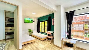 Une chambre comprenant un lit, un bureau, une chaise, une télévision et une fenêtre donnant sur des immeubles.