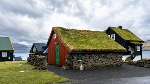 A traditional Icelandic house with a grass roof, stone walls, and a red door. - Traditional Cabin with Sea View (Stykkið)