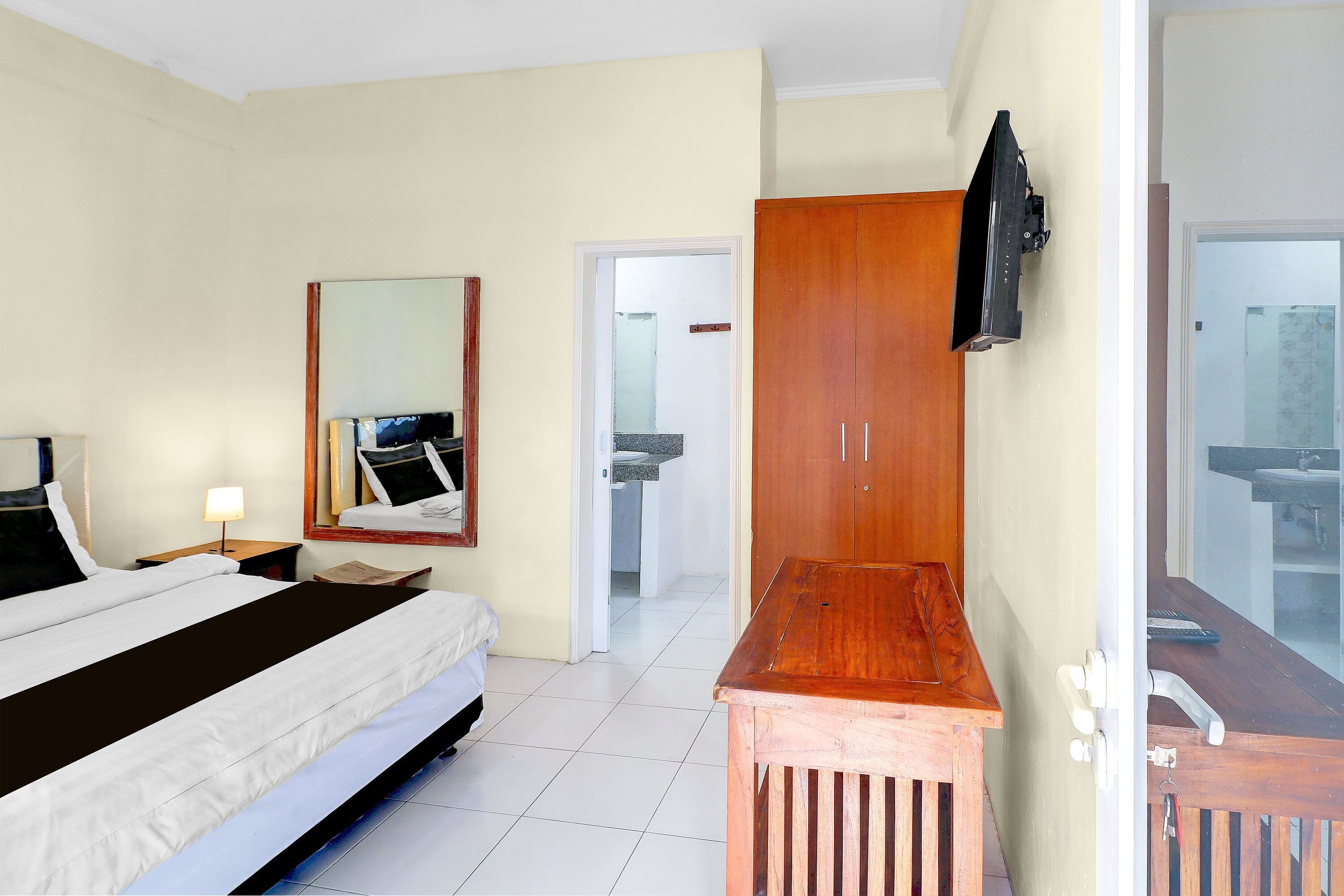 A hotel room with a bed, a wooden desk, a television mounted on the wall, and a bathroom visible through an open door.