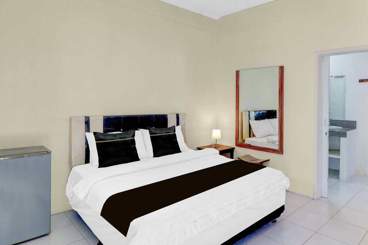 Ein Hotelzimmer mit einem Bett, einem Nachttisch, einem Spiegel und einer Tür zu einem Badezimmer.
