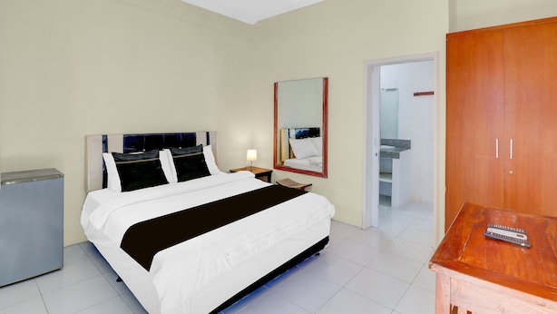 Habitación de hotel con cama, mesita de noche, lámpara, armario y un pequeño escritorio con un control remoto.