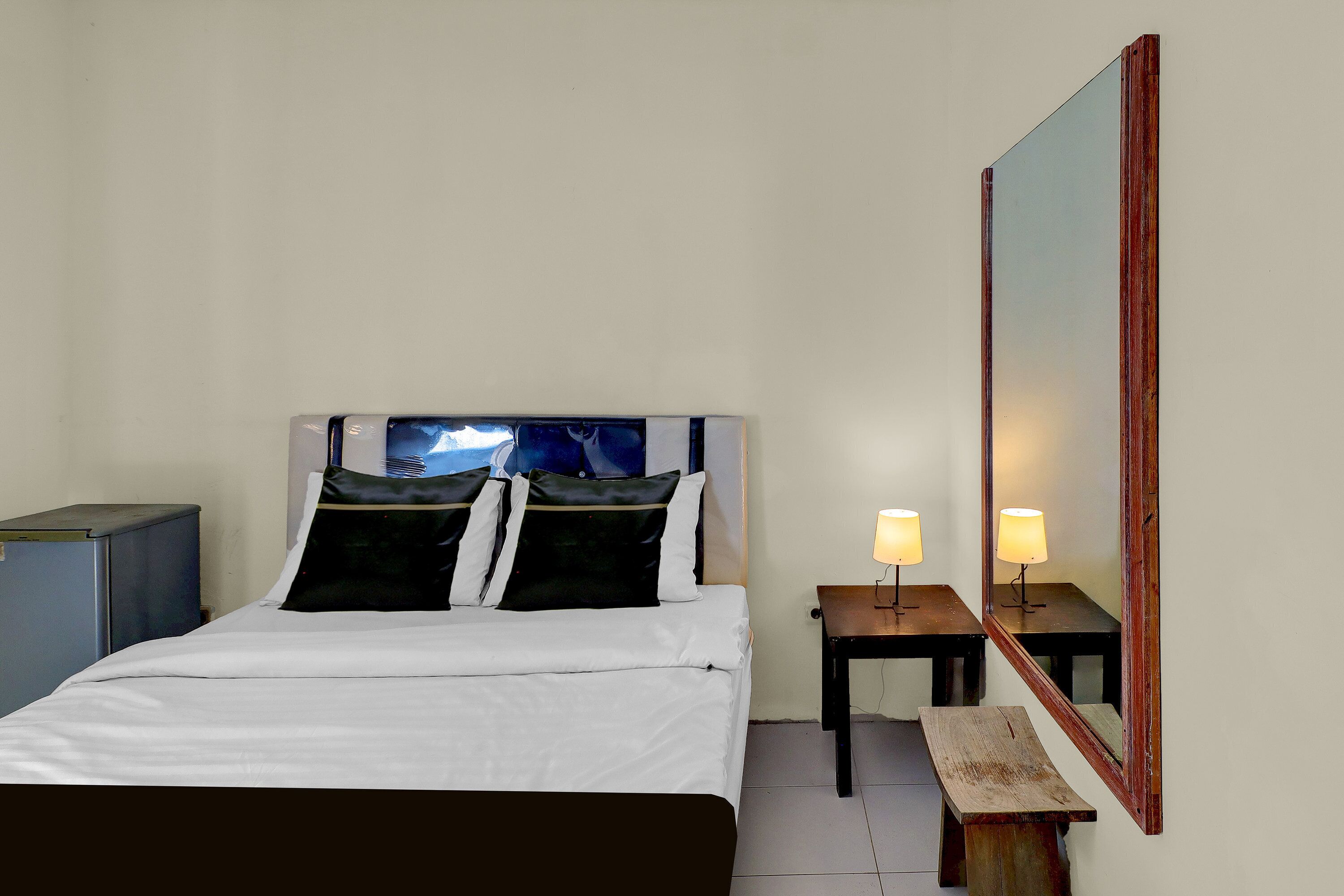 Habitación de hotel con cama, mesita de noche con lámpara, una pequeña mesa y un espejo grande.