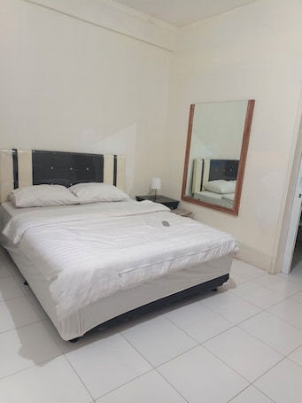 A clean, well-lit hotel room with a large bed, a bedside table, a nightstand, and a mirror on the wall.. Hotel O near Kuta Beach formerly Cozy Ro