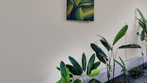 Pared con un cuadro de flores rosadas y hojas verdes, y una planta en maceta con hojas grandes.
