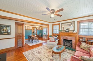 A spacious living room with hardwood floors, a ceiling fan, a fireplace, and a dining area.