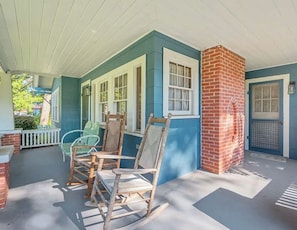 A porch with a brick column, a rocking chair, and a table.