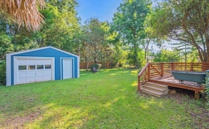 A backyard with a blue shed, a wooden deck, and a lawn.