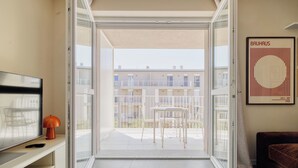 Ein Zimmer mit einer Schiebetür zu einem Balkon im Freien, der weiße Stühle und einen Tisch bietet.