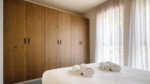 Ein Schlafzimmer mit einem großen Holzschrank, einem ordentlich bezogenen Bett und leichten Vorhängen.