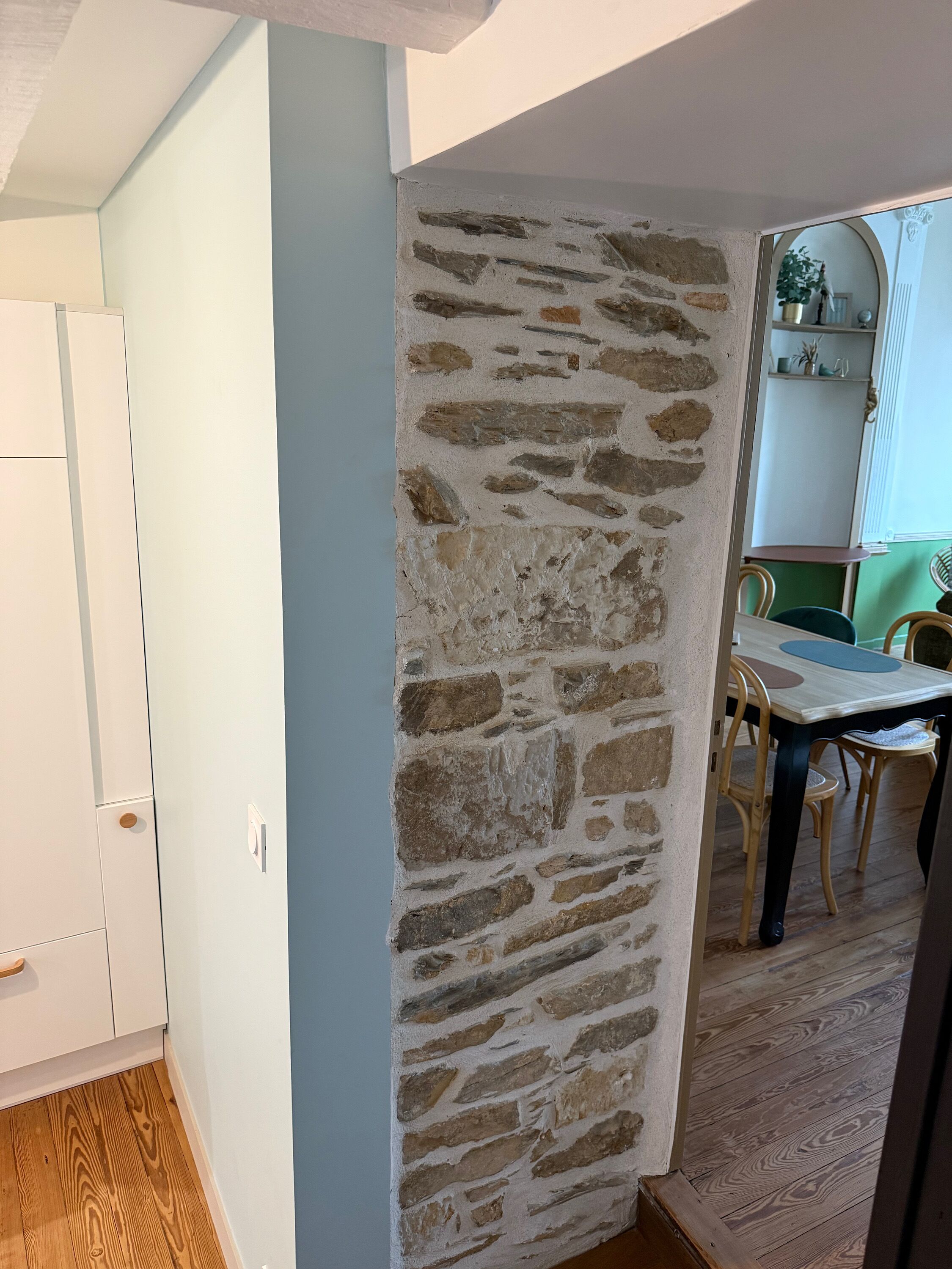 A room with a stone wall, wooden flooring, a white cabinet, and a dining area with a table and chairs.