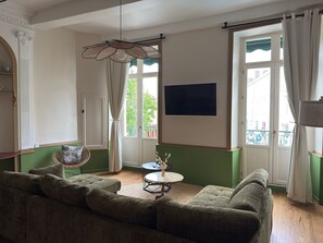 A living room with a sofa, a table, a hanging light fixture, and a large window with curtains.