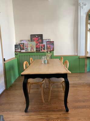 A dining table with chairs, framed artwork on the wall, and a radiator. - Charming apartment ideal for family, friends or business. (Château-Gontier-sur-Mayenne)