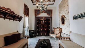 Ein traditionell eingerichteter Raum mit Sofa, Couchtisch, Sessel, einer Chandelüster und einer großen, verzierten Tür.