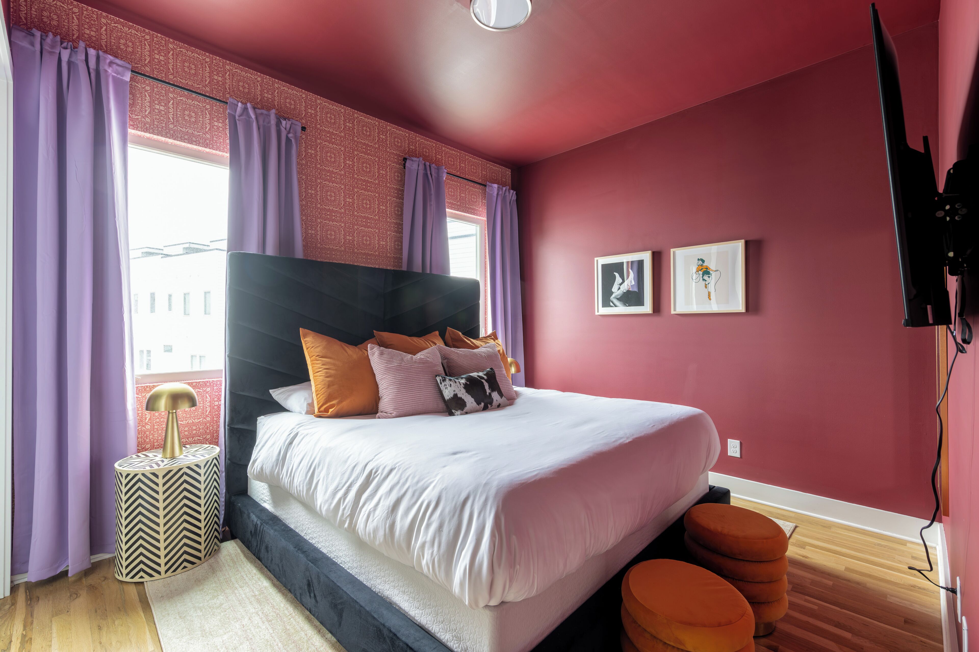 Une chambre à coucher avec un lit, une table de chevet, une télévision et une fenêtre avec des rideaux.