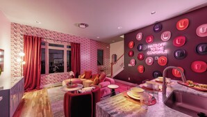 Una sala de estar moderna con un sofá rosa, un comedor con una mesa de mármol y una pared decorada con sombreros.