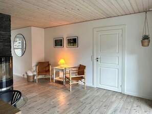 Une pièce avec un plafond en bois, une porte blanche, une table avec des chaises, une lampe et des tableaux encadrés accrochés au mur.