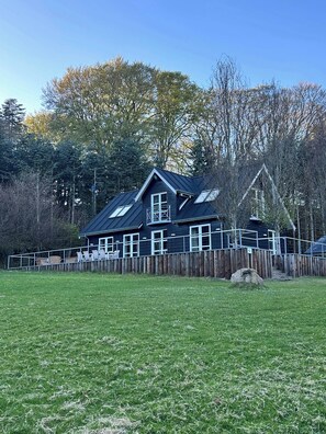 Een huis met twee verdiepingen, een donker dak, meerdere ramen en een omheinde tuin.